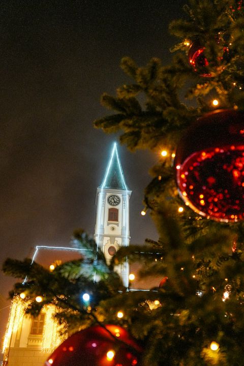 En upplyst julgran på ett torg framför en kyrka.